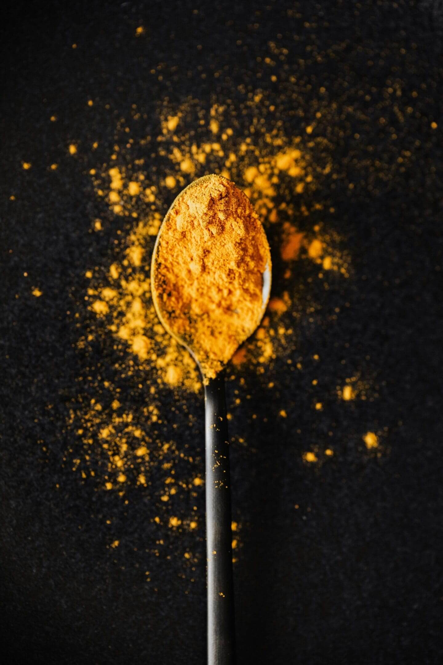 A spoon filled with vibrant turmeric powder against a dark background.